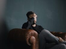 a man holds his head while sitting on a sofa