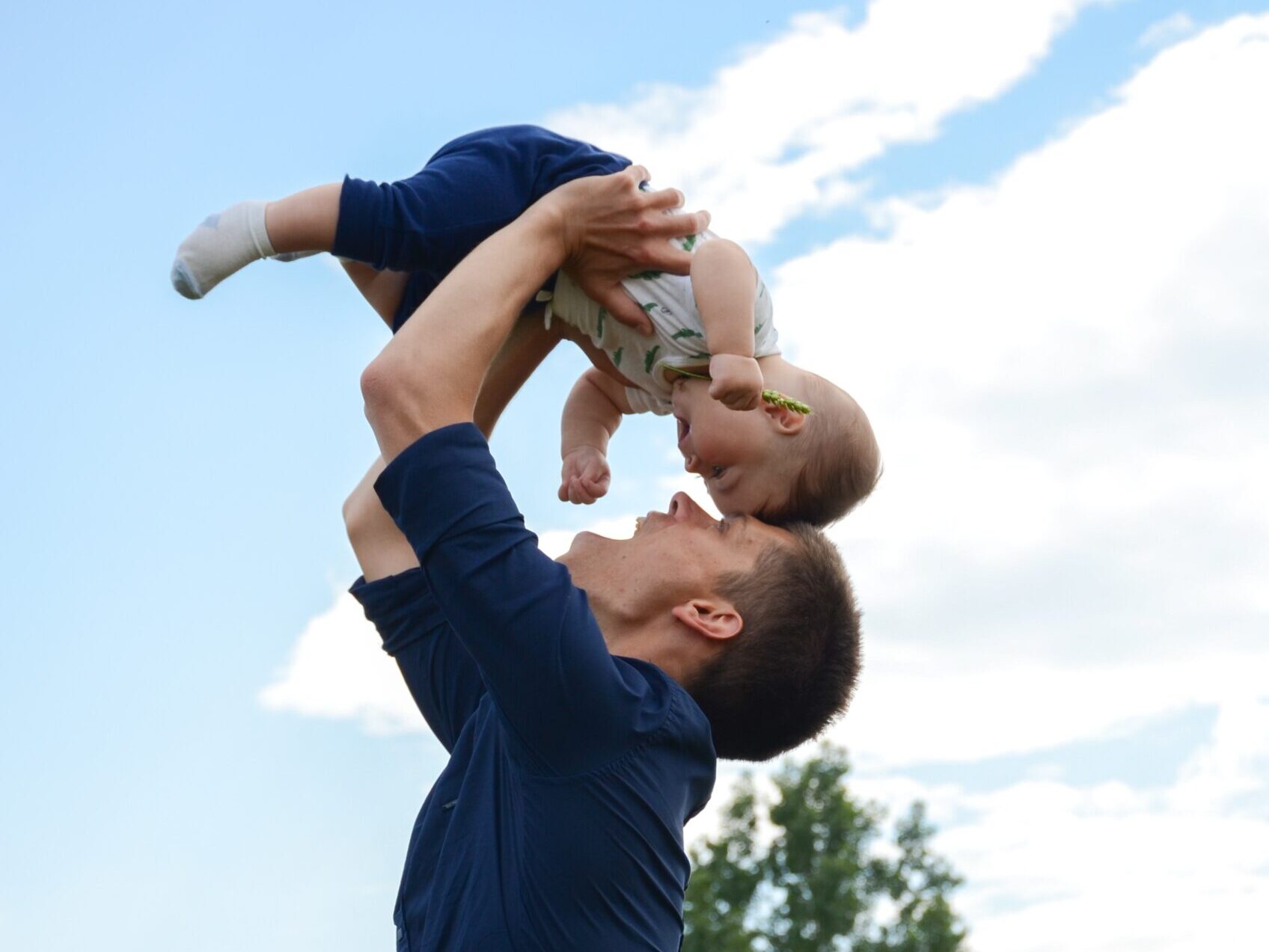 man in blue long sleeve shirt carrying baby in white onesie