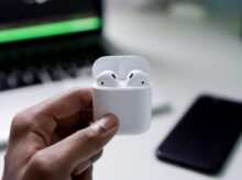 person holding wireless earbuds with charging case