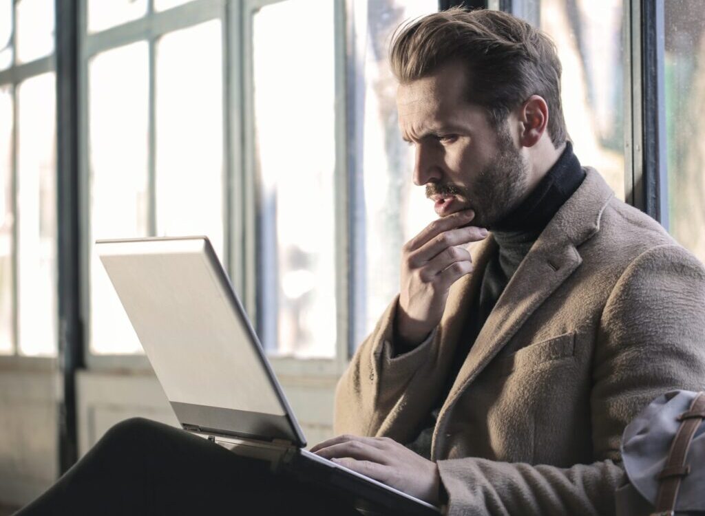man holding his chin facing laptop computer