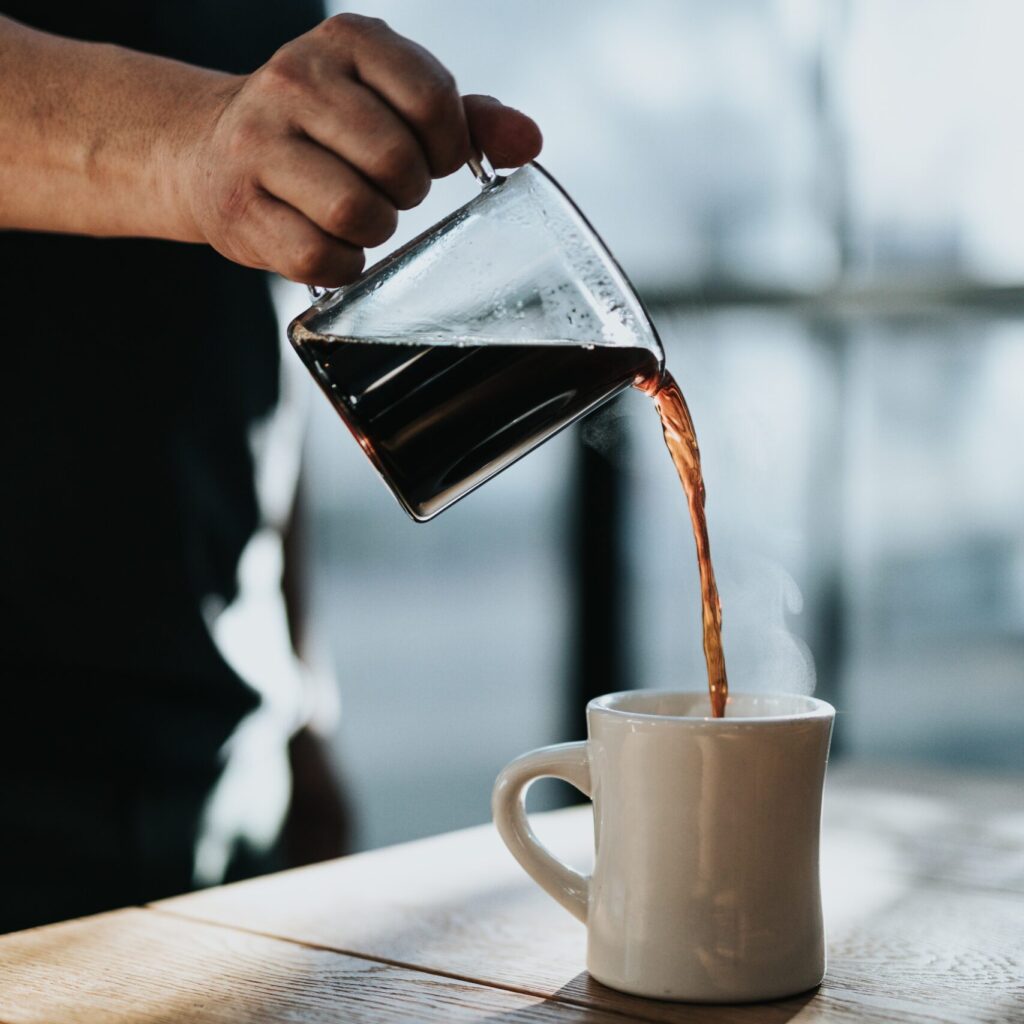 person pouring black coffee in white ceramic mug placed on brown wooden table during daytime
