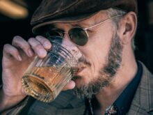 man in black and white plaid suit jacket holding clear drinking glass