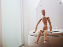 brown wooden doll on white ceramic toilet bowl