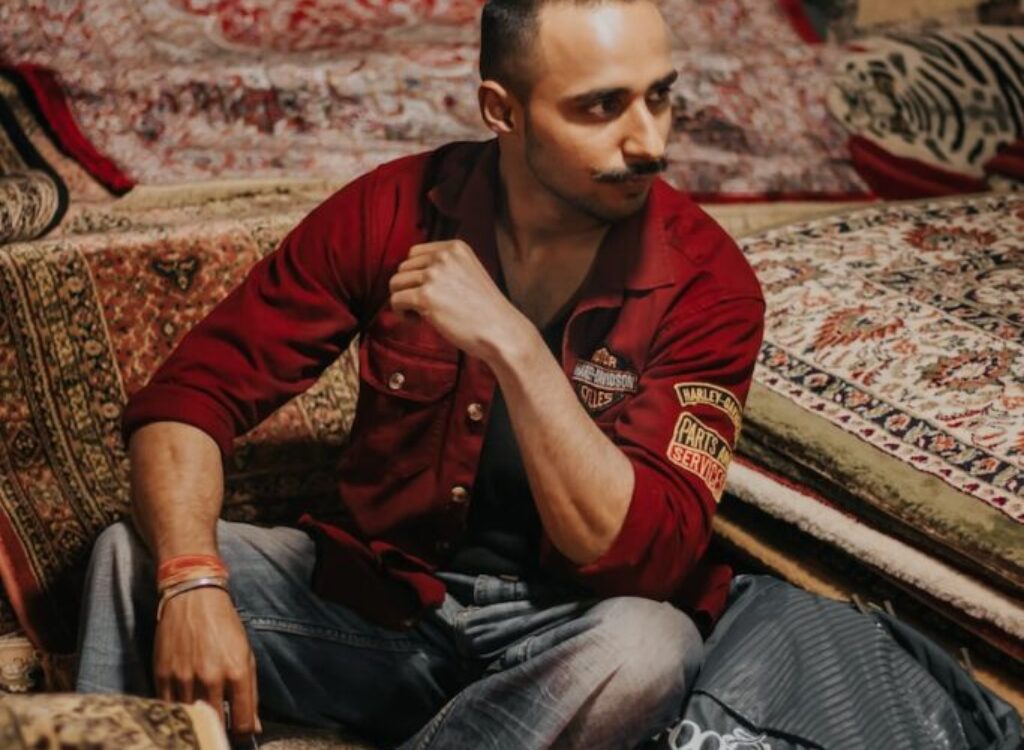 man in red polo shirt and blue denim jeans sitting on brown and beige floral couch