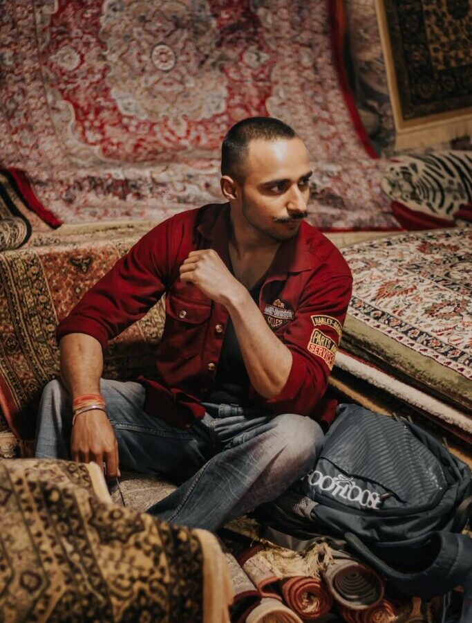 man in red polo shirt and blue denim jeans sitting on brown and beige floral couch