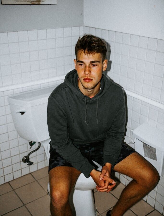 man in black hoodie sitting on toilet bowl