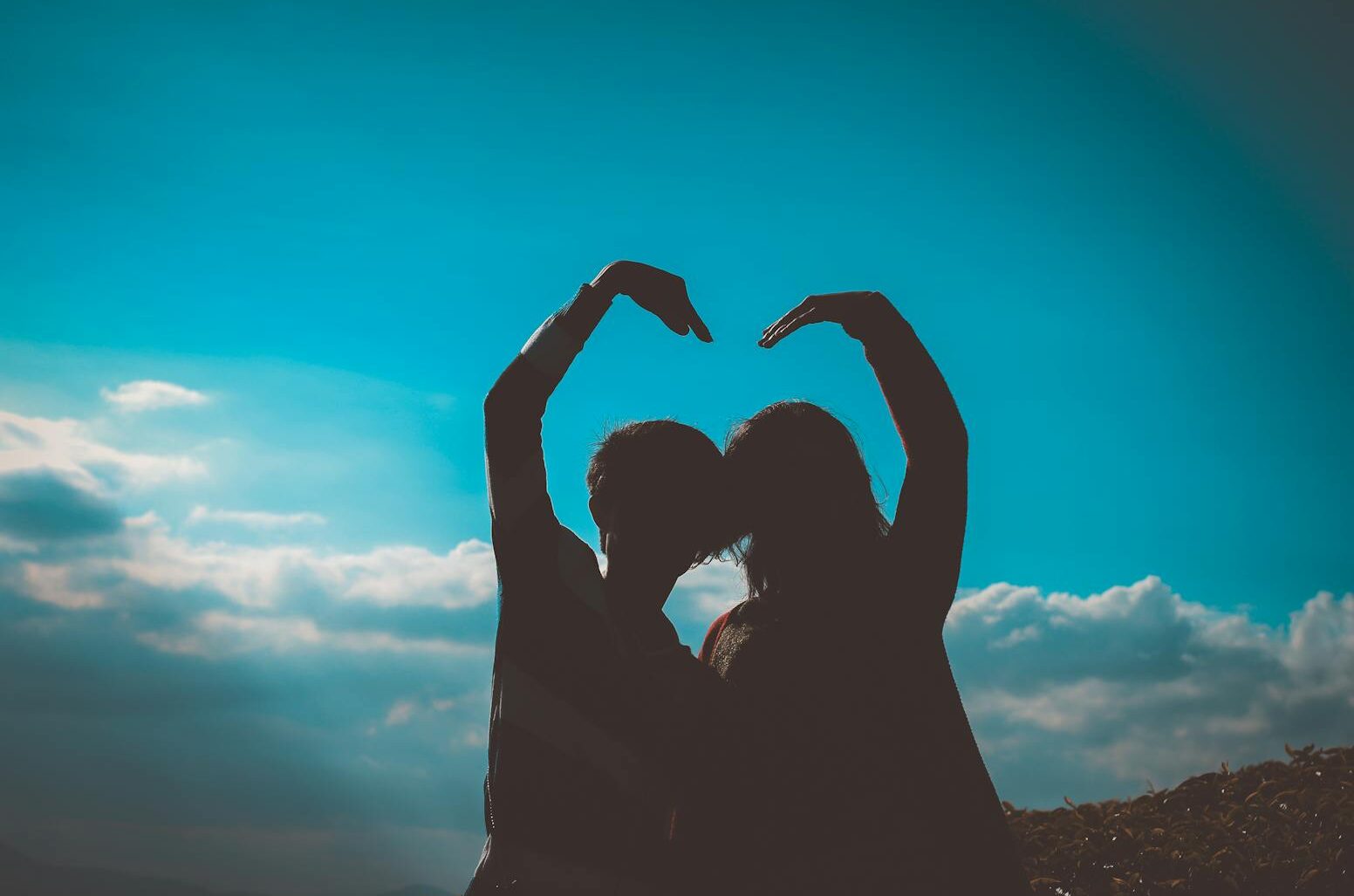 Silhouette of a couple creating a heart shape with their arms in a romantic outdoor setting.